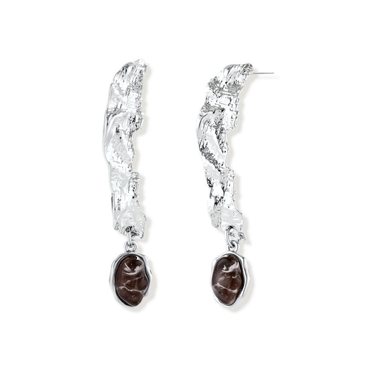 Silver-toned twisted metal earrings with dark brown oval resin stones dangling from sculptural posts on white background.