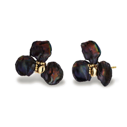 Dark iridescent baroque pearls arranged in flower pattern with 18K gold-plated center on cream background.