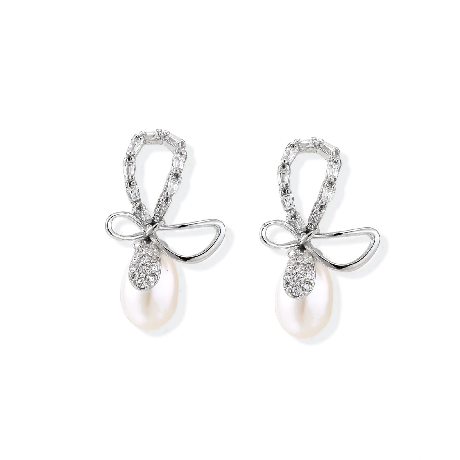 Silver bow-shaped stud earrings with baguette crystals and dangling white freshwater pearls on cream background
