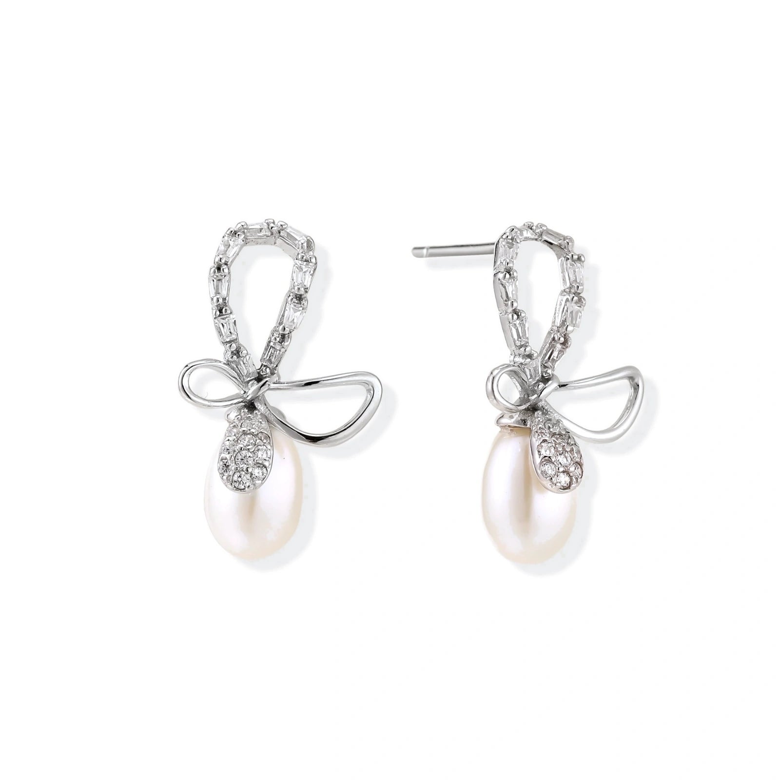 Silver bow-shaped stud earrings with baguette crystals and dangling white freshwater pearls on cream background