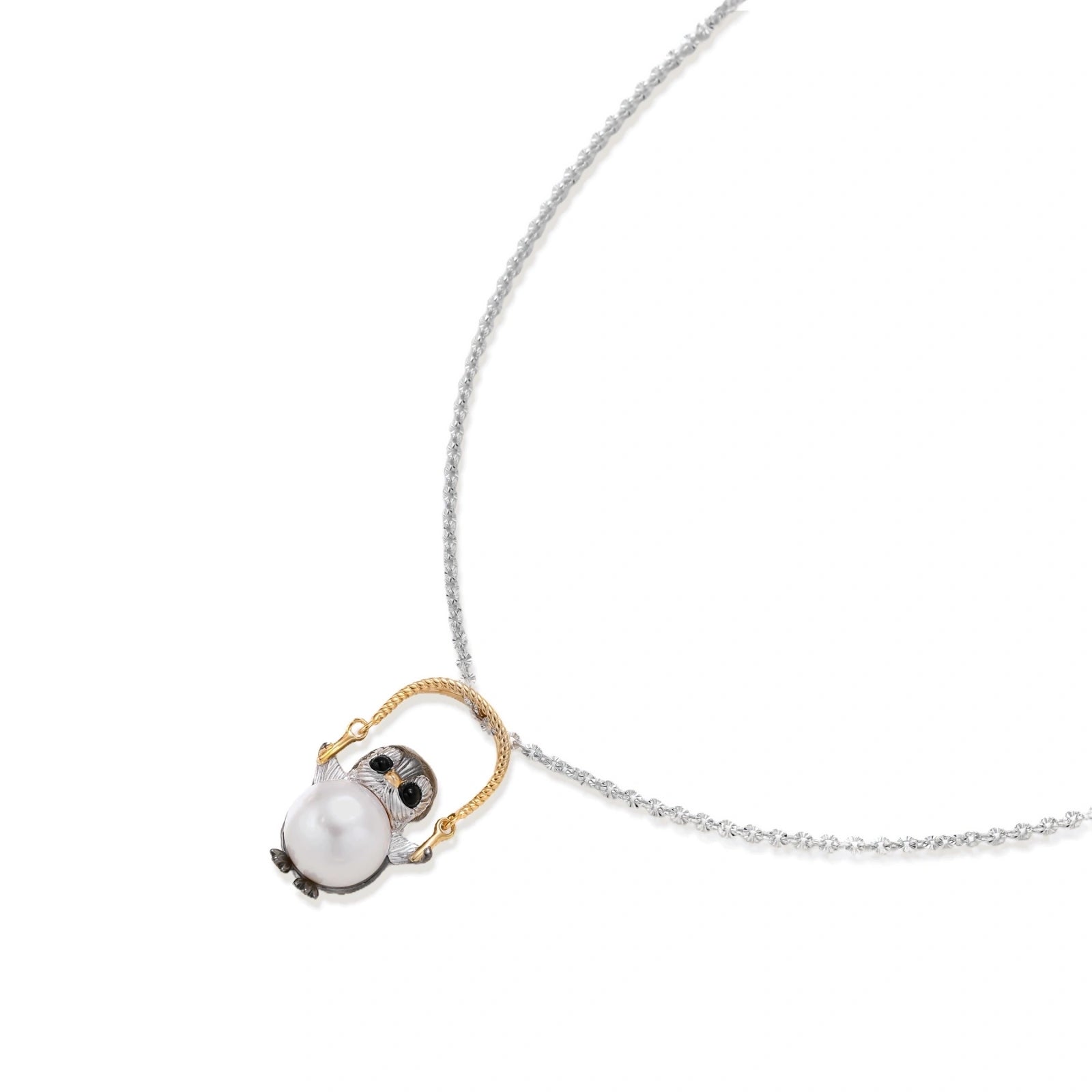 Whimsical penguin pendant holding a white pearl on a gold swing, rhodium-plated silver chain on cream background.