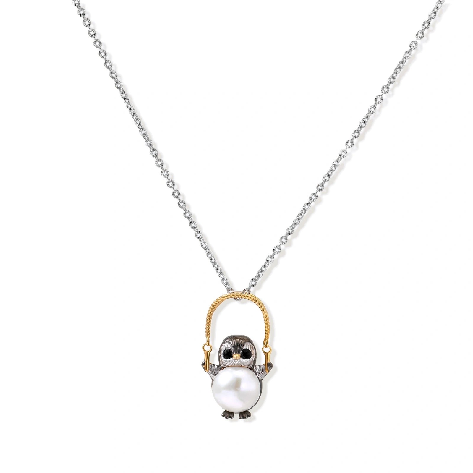 Whimsical penguin pendant holding a white pearl on a gold swing, rhodium-plated silver chain on cream background.