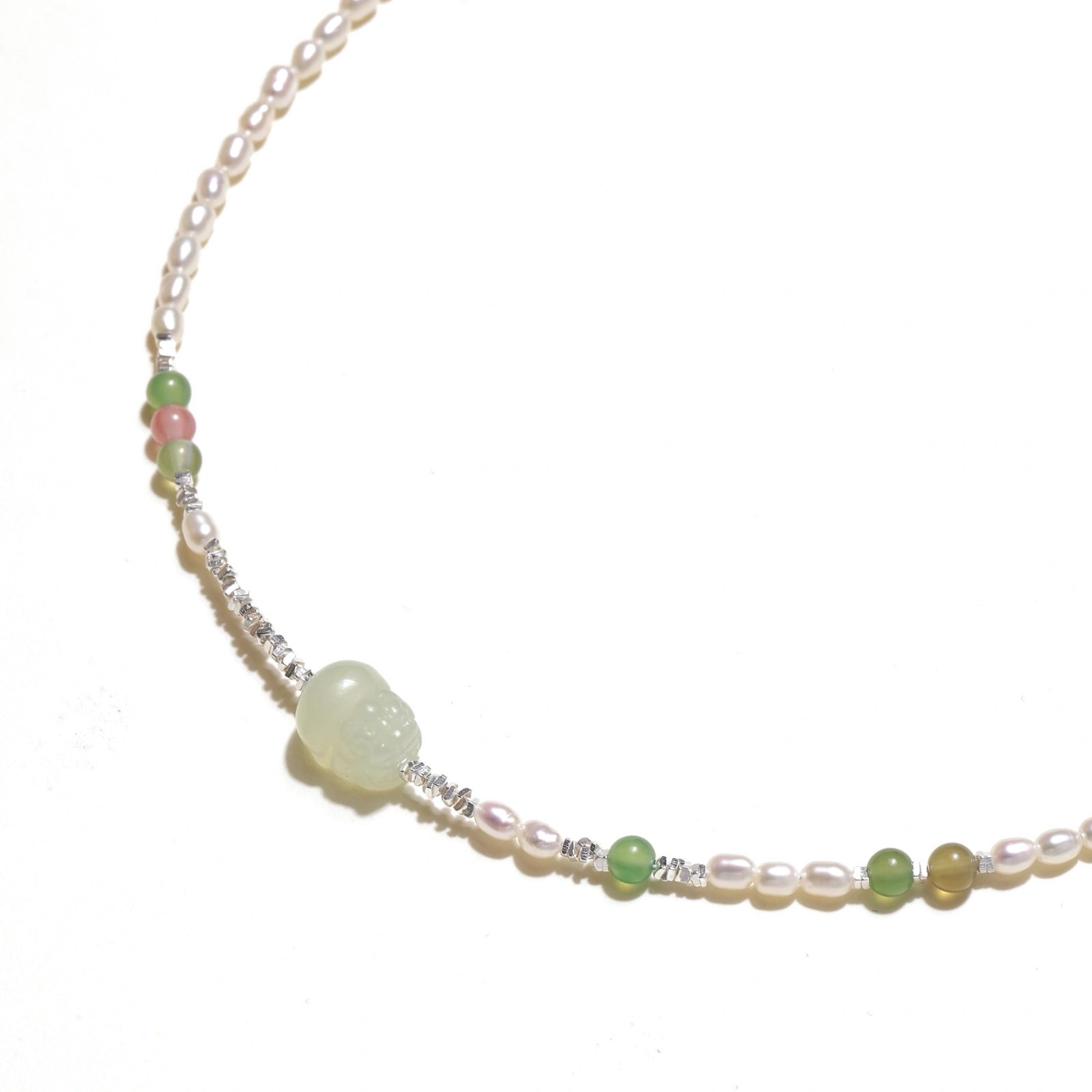 Delicate pearl necklace with pale green serpentine jade centerpiece and colorful agate beads on cream background