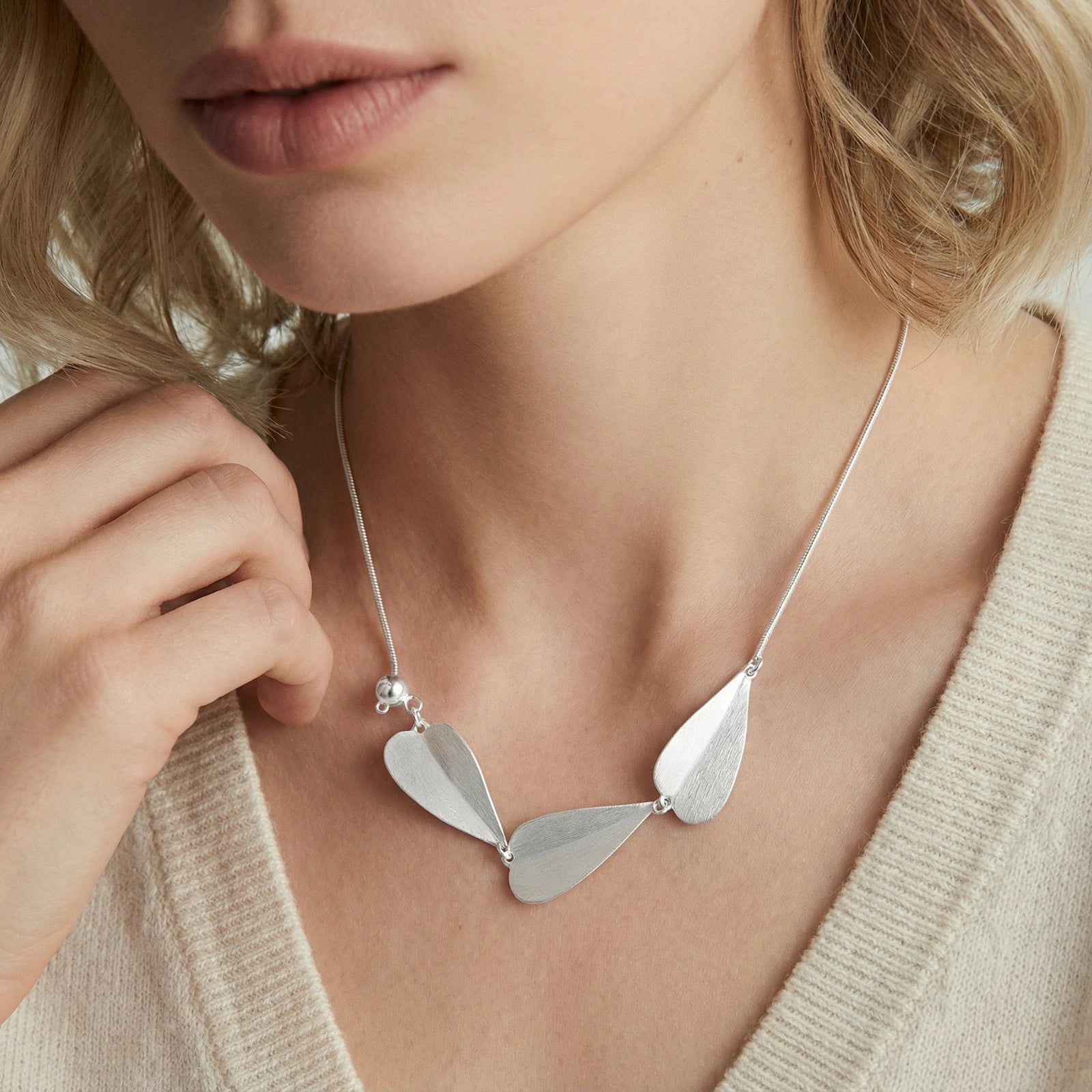 Close-up of a woman wearing the Botanical Whisper Necklace featuring three delicate sterling silver leaf-shaped pendants on a thin chain, paired with a neutral knit top.