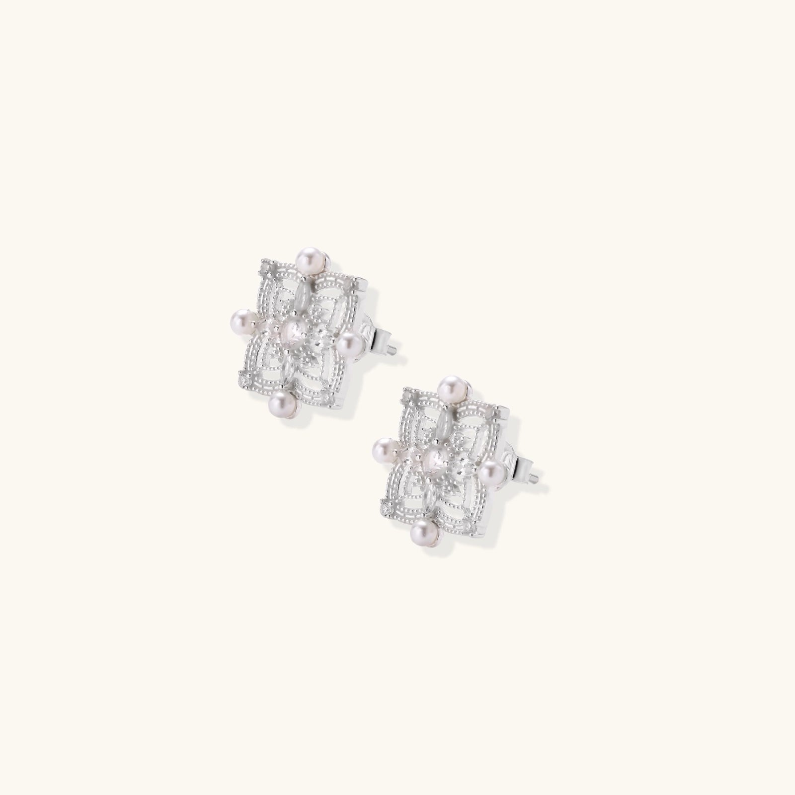 Ornate sterling silver stud earrings with mandala-inspired filigree pattern and four freshwater pearls on beige background
