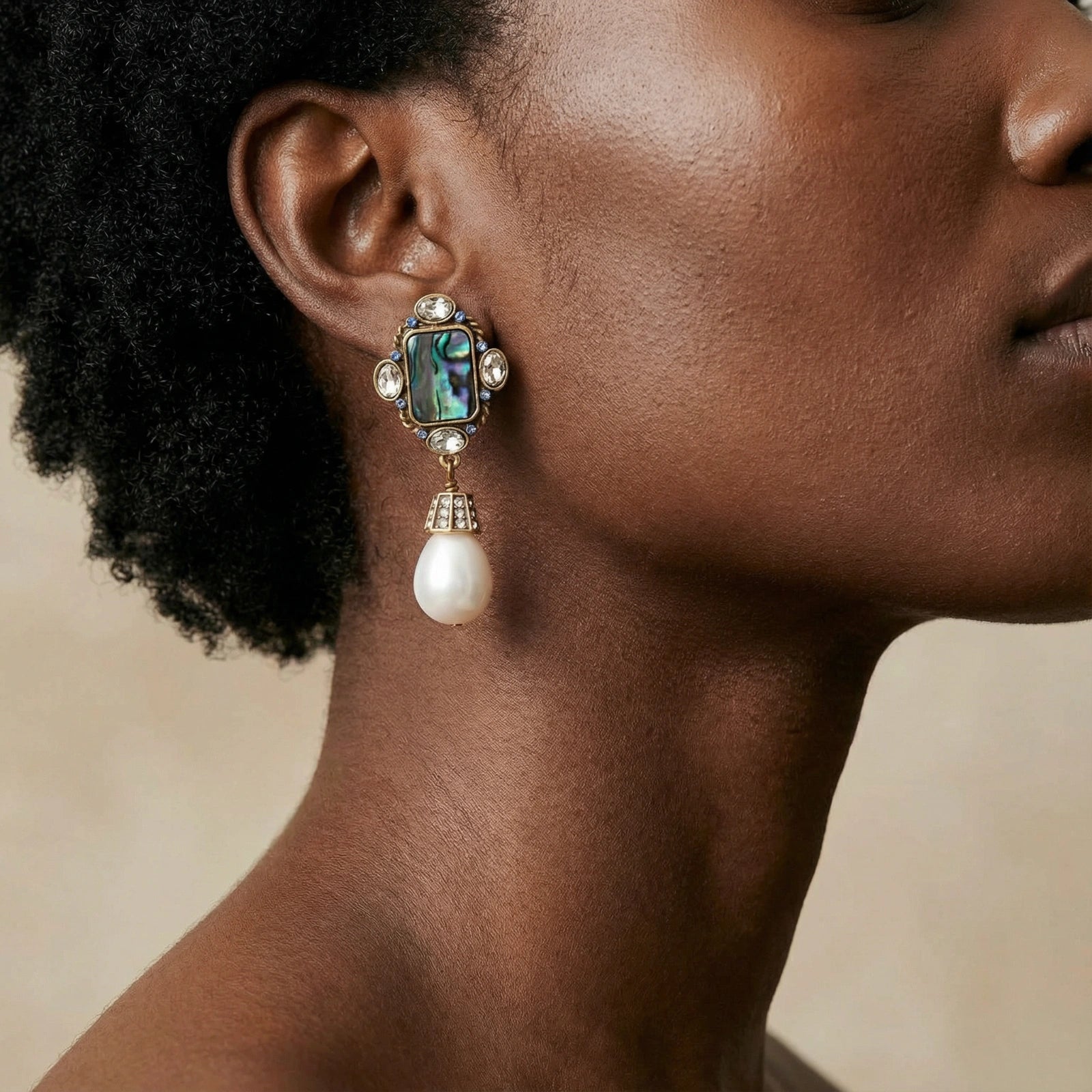 Close-up of a woman's ear wearing Pearl Drop Earrings featuring a 14K gold plated setting with a rectangular abalone shell and a hanging baroque pearl drop.
