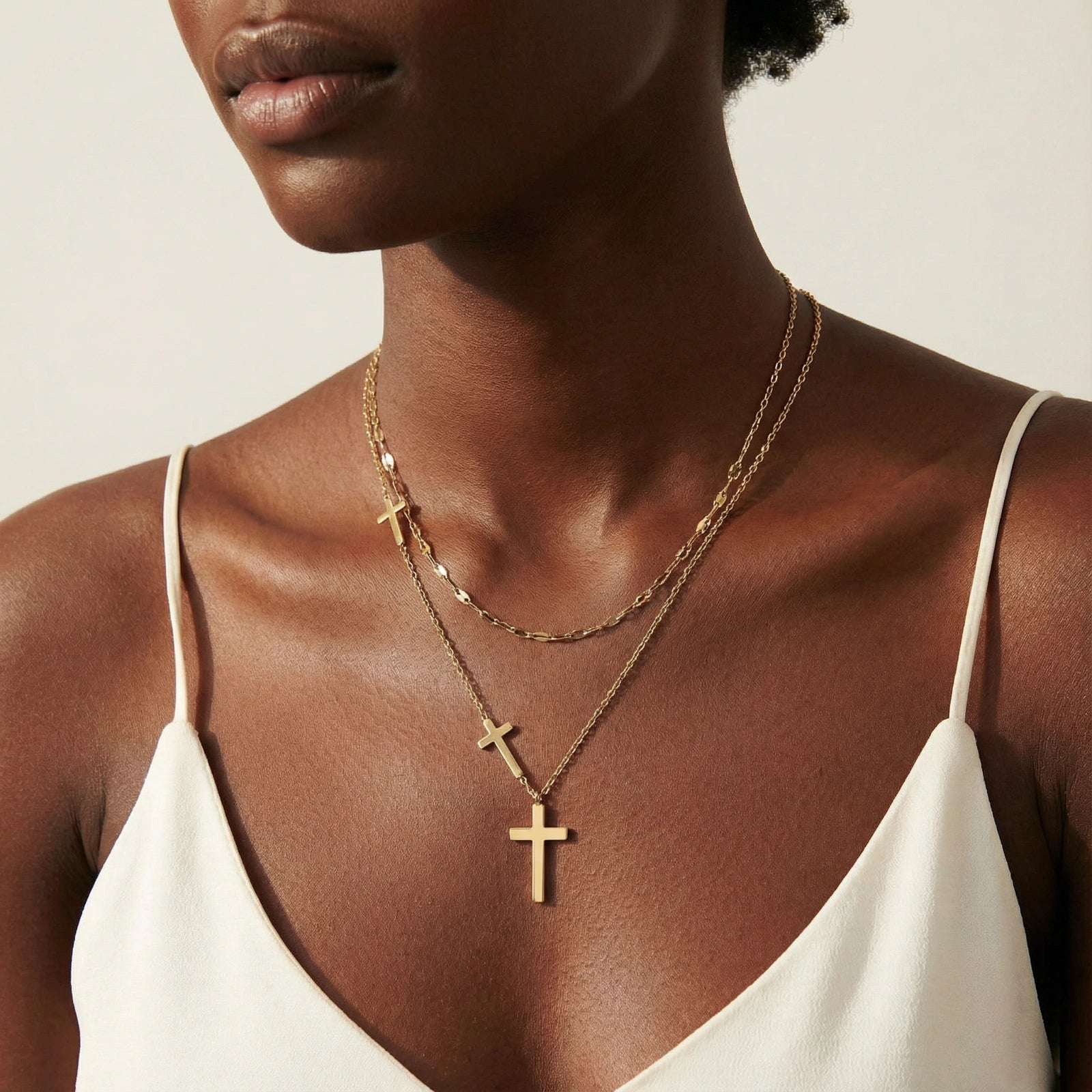 Close-up of a woman wearing the Layers Necklace Set featuring two delicate 14K gold plated chains with simple cross pendants, styled with a white sleeveless top.