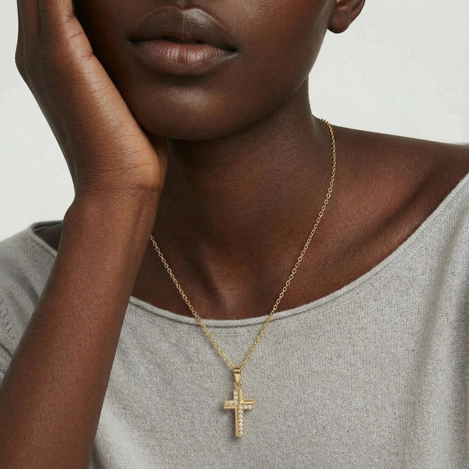 Close-up of a person wearing the Radiance Necklace, a delicate 14K gold plated cross pendant on a fine chain, styled with a casual light grey top.