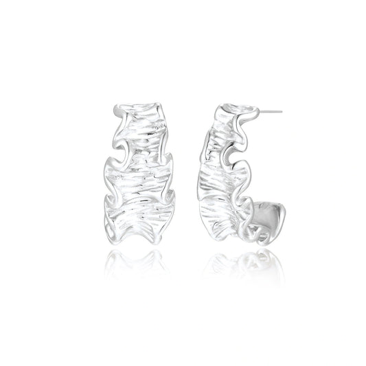 White gold plated sculptural hoop earrings with organic wavy edges and reflective metallic finish on cream background