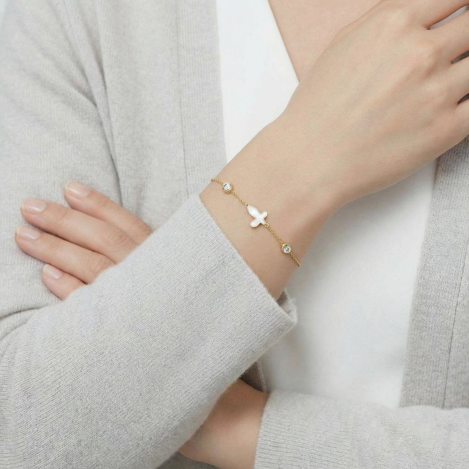 Bracelet featuring a delicate 14K gold plated chain with a small baroque pearl charm, worn on the wrist over a light grey cardigan and white top, showcasing elegant luxury jewelry.