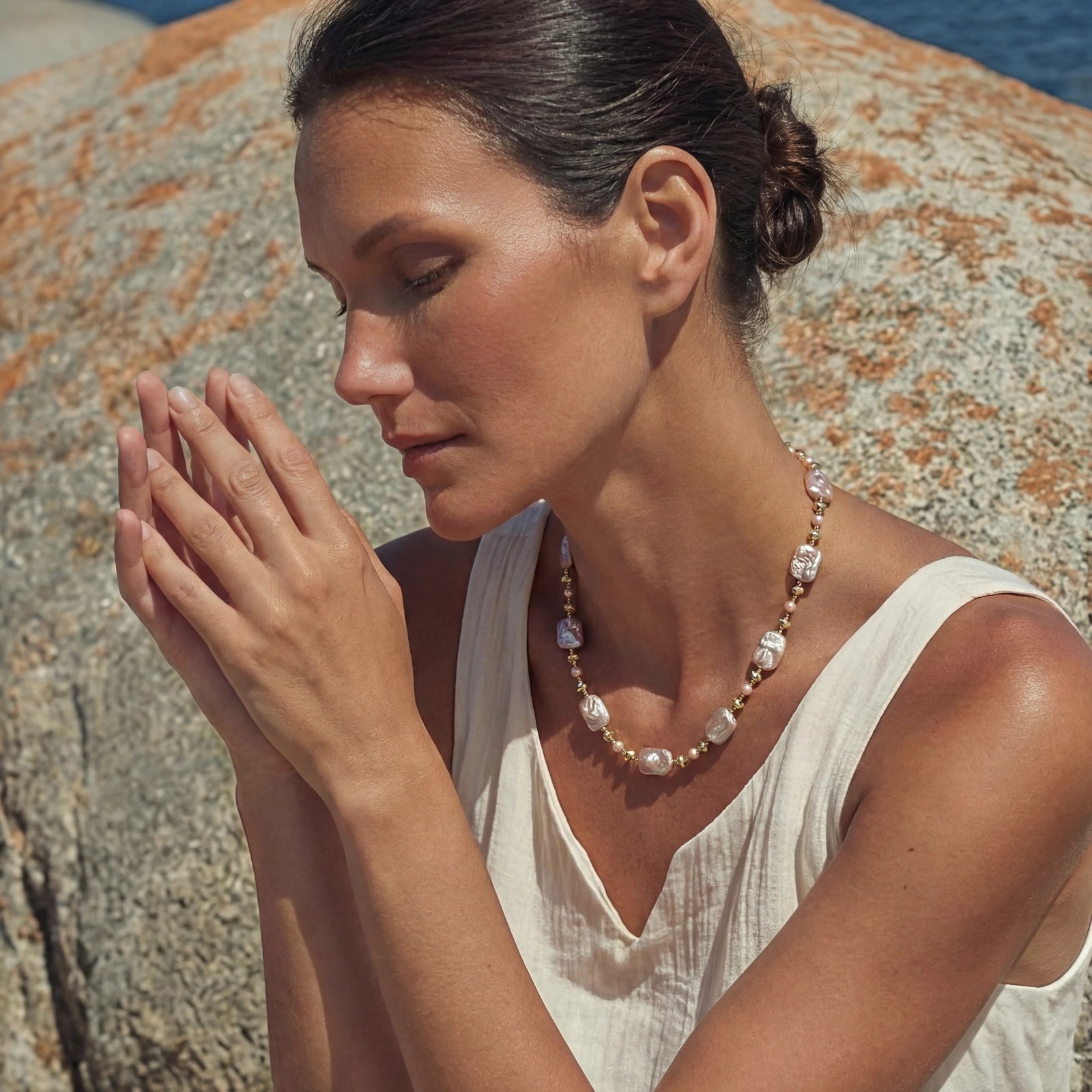 Woman wearing an Iridescent Pearl Chain necklace made of 14K gold plated and sterling silver, styled with a white sleeveless top against a natural rocky background.