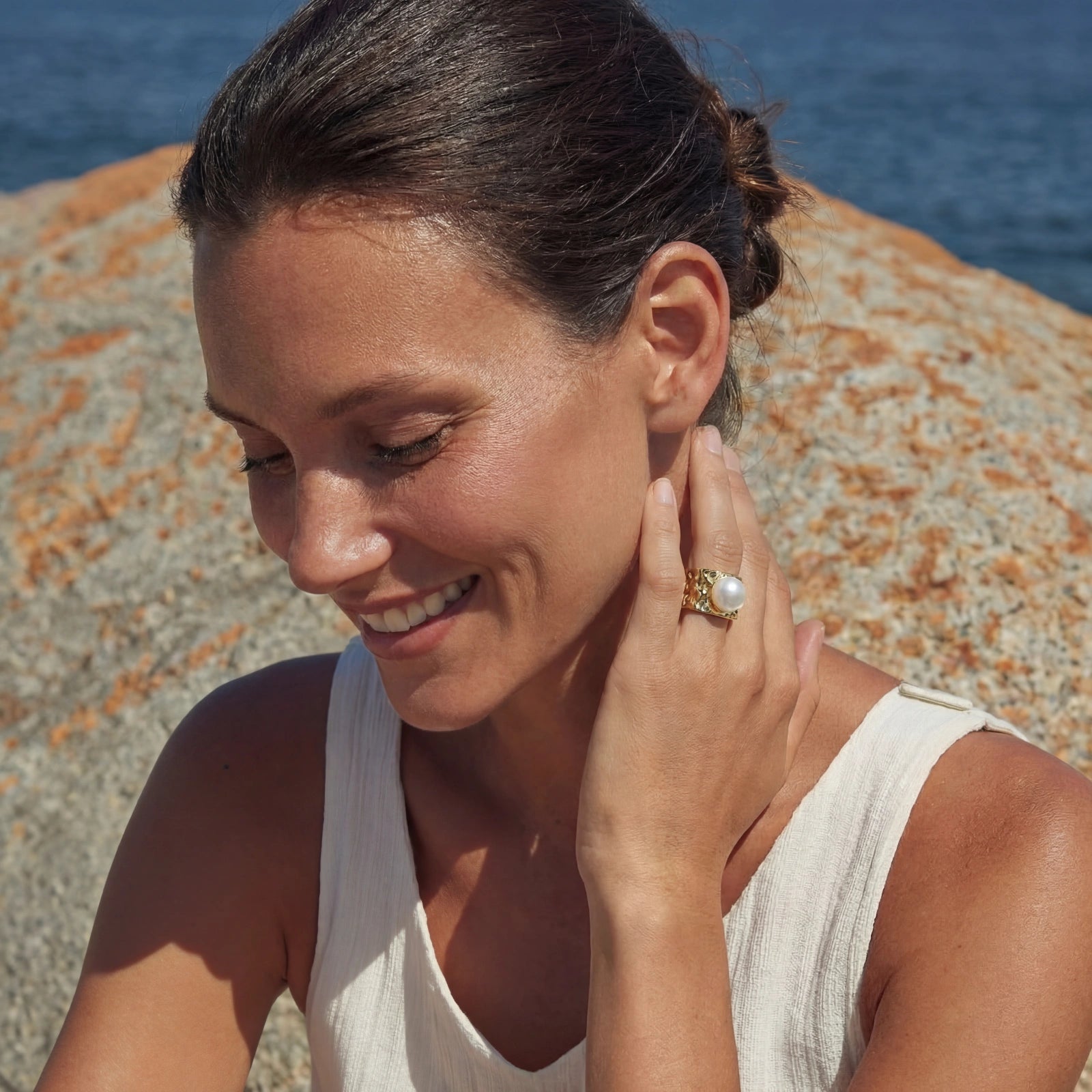 Woman wearing the Golden Tide Pearl Ring, a 14K gold plated piece with a prominent pearl, posing outdoors near the sea with a natural smile.