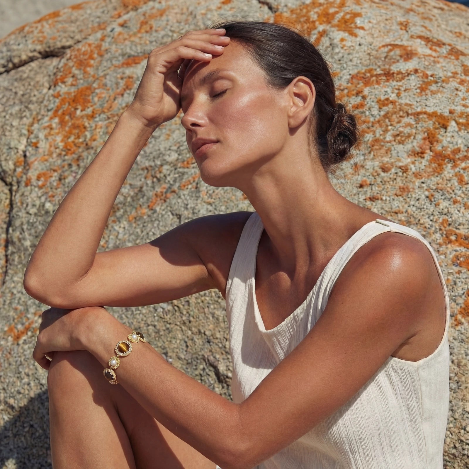 Woman wearing a Tiger's Eye Pearl Wisdom Bracelet made with 14K gold plated and sterling silver, posing outdoors against a textured rock background.