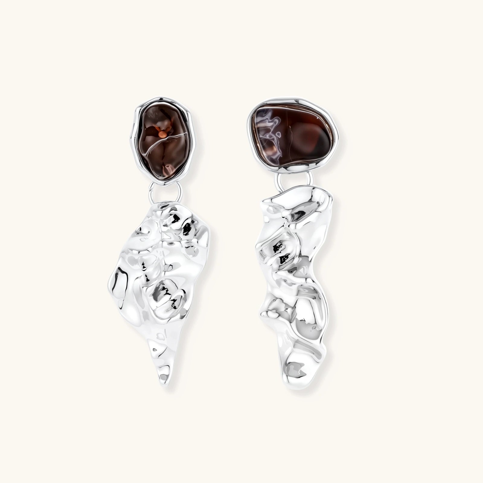 Abstract sculptural silver earrings with brown resin stones featuring organic fluid metalwork design on white background.