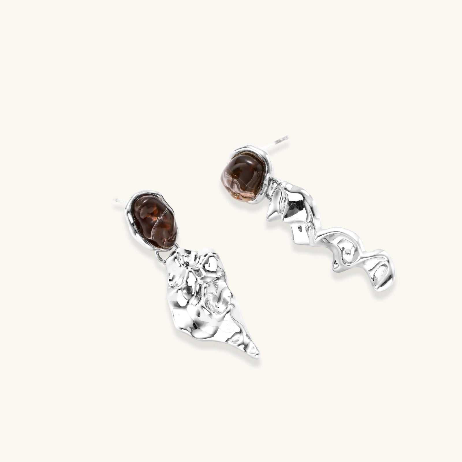 Abstract sculptural silver earrings with brown resin stones featuring organic fluid metalwork design on white background.