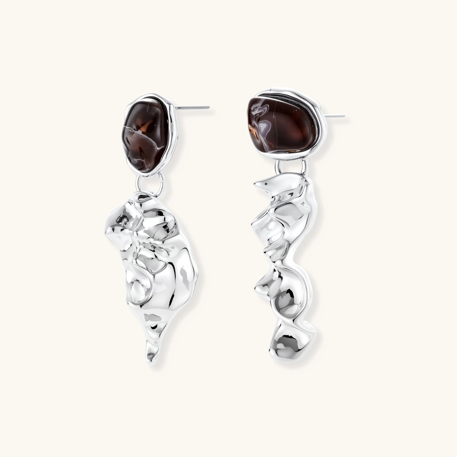 Abstract sculptural silver earrings with brown resin stones featuring organic fluid metalwork design on white background.